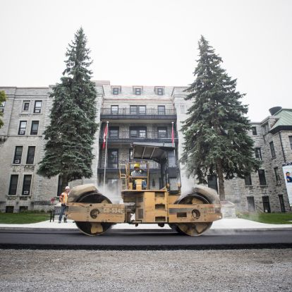 A roller flattens hot, fresh asphalt on Stuart Street in front of the Watkins wing entrance.