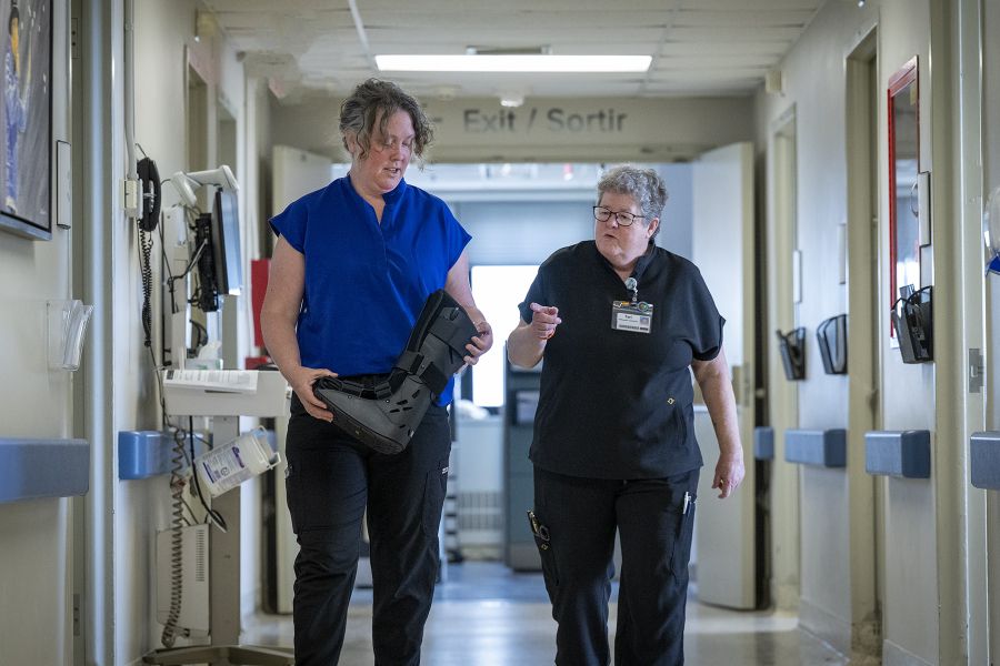 Teri Timpany is walking and talking with a colleague down a hallway. The colleague is holding an Aircast boot and Teri is pointing at it.