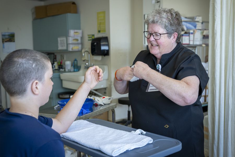 A shot of Teri Timpany having a discussion with a young patient, as she walks him through the casting process. Teri has short, curly, silver hair and wears glasses. She’s wearing black scrubs.